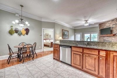 kitchen with sink, dishwasher, dark stone countertops, ceiling fan with notable chandelier, and ornamental molding