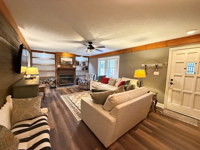 living room featuring dark wood-type flooring, a large fireplace, ceiling fan, and a textured ceiling