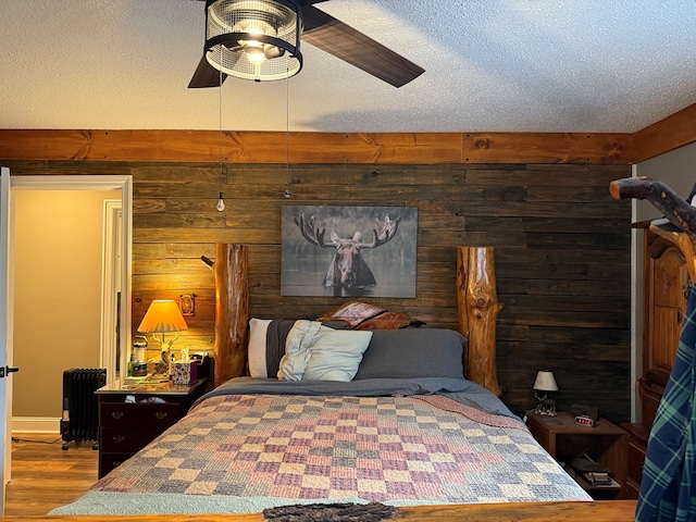 bedroom featuring wood-type flooring, a textured ceiling, radiator heating unit, wooden walls, and ceiling fan