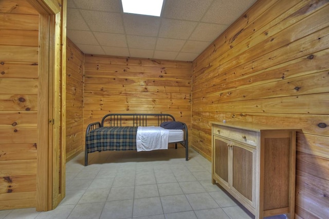 unfurnished bedroom with light tile floors, wooden walls, and a drop ceiling