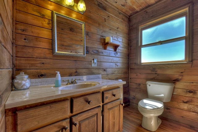 bathroom with toilet, wood-type flooring, wood walls, and vanity