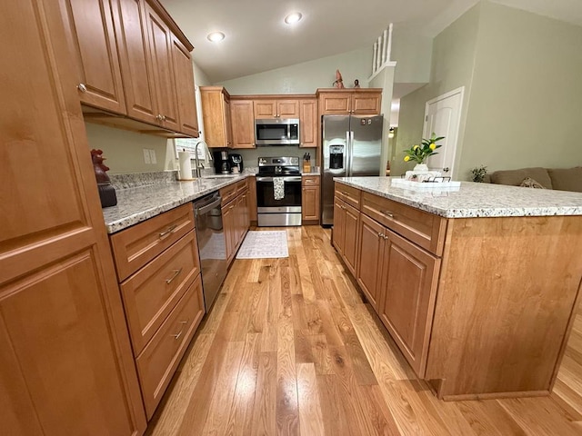 kitchen featuring appliances with stainless steel finishes, light wood-style floors, lofted ceiling, a center island, and light stone counters