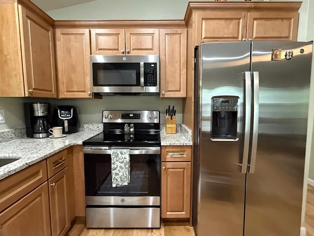 kitchen with stainless steel appliances, light stone counters, light wood-style floors, and brown cabinets