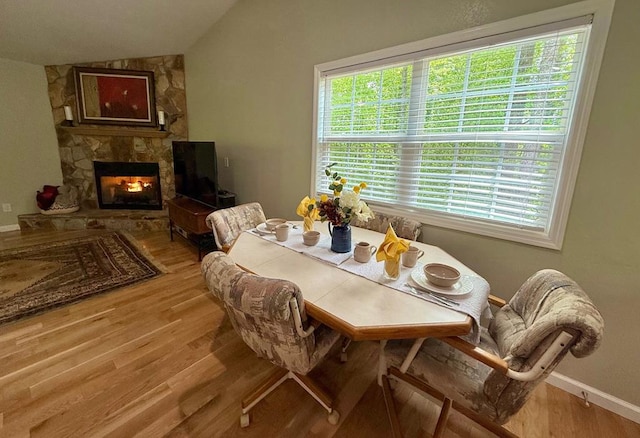dining area featuring lofted ceiling, wood finished floors, a fireplace, and baseboards