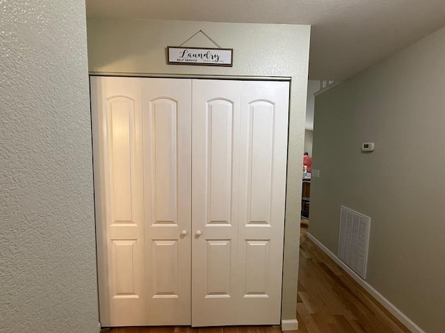 detailed view of wood finished floors, a textured wall, and baseboards