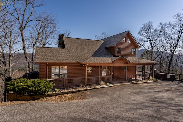 rustic home featuring faux log siding, covered porch, driveway, and a shingled roof