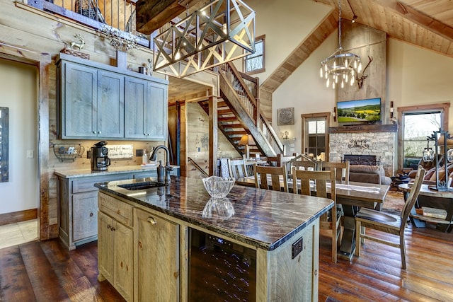 kitchen featuring beverage cooler, beam ceiling, a stone fireplace, high vaulted ceiling, and a sink