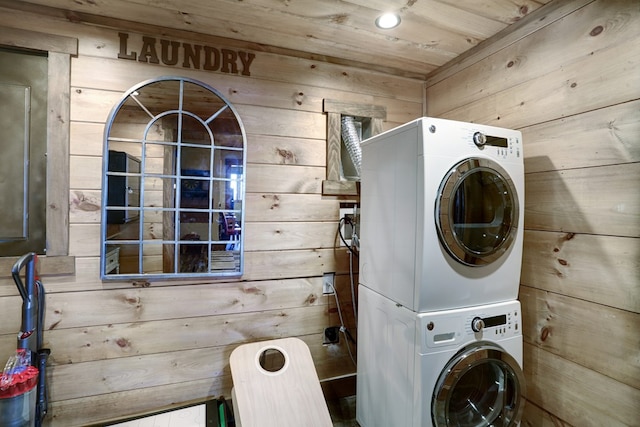 laundry area featuring stacked washer / drying machine, wood walls, and laundry area