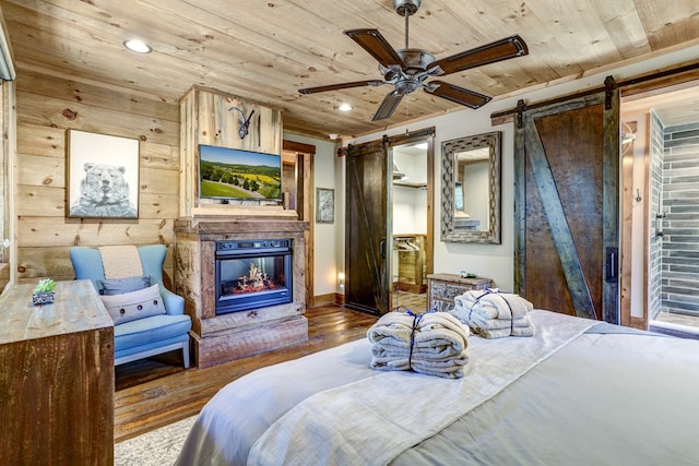 bedroom featuring a glass covered fireplace, a barn door, wood finished floors, and wooden ceiling