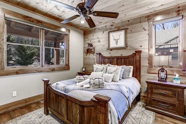 bedroom featuring hardwood / wood-style floors, wooden walls, wooden ceiling, baseboards, and ceiling fan