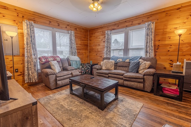 living room featuring a wealth of natural light, wooden walls, ceiling fan, and light wood-type flooring