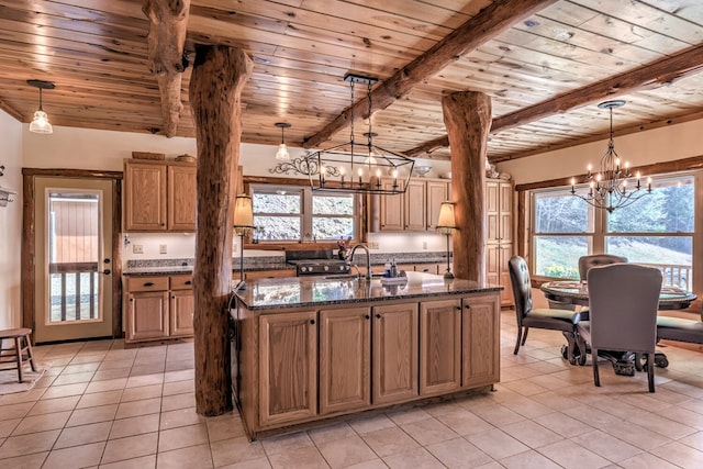 kitchen with dark stone counters, hanging light fixtures, a kitchen island with sink, and an inviting chandelier