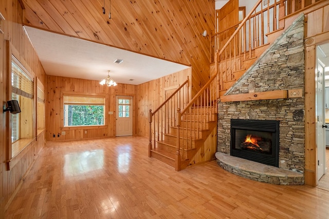 unfurnished living room featuring a stone fireplace, a towering ceiling, an inviting chandelier, wooden walls, and light wood-type flooring