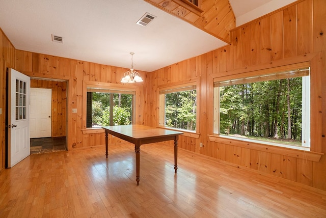 unfurnished dining area featuring a notable chandelier, light hardwood / wood-style floors, and wood walls