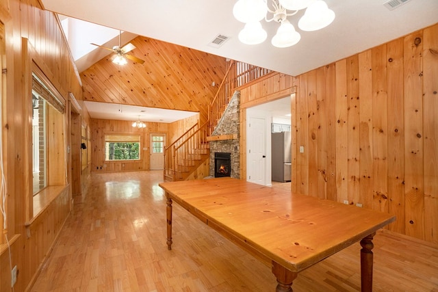 interior space with ceiling fan with notable chandelier, high vaulted ceiling, a fireplace, wood walls, and light wood-type flooring