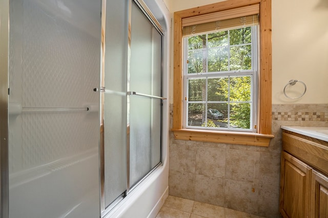 bathroom with tile walls, vanity, tile patterned floors, and combined bath / shower with glass door