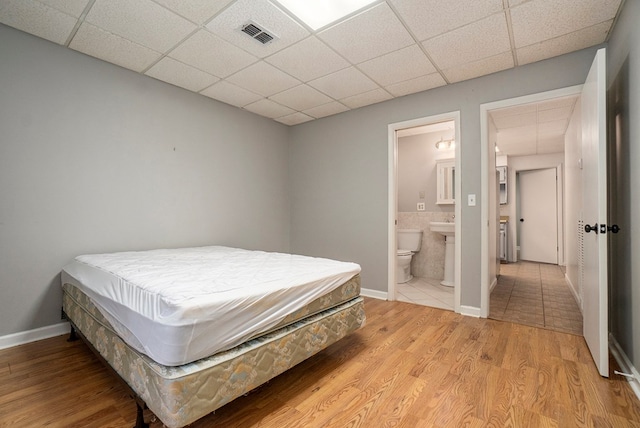 bedroom featuring ensuite bathroom, a paneled ceiling, and light hardwood / wood-style floors