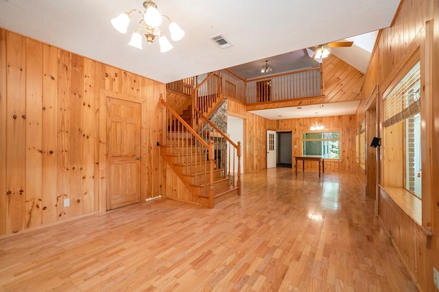 unfurnished living room featuring a high ceiling, ceiling fan with notable chandelier, hardwood / wood-style floors, and wood walls