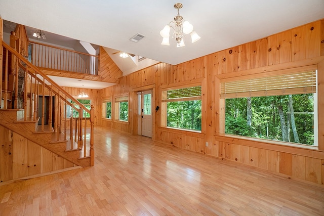 unfurnished living room with high vaulted ceiling, wooden walls, a chandelier, and light hardwood / wood-style floors