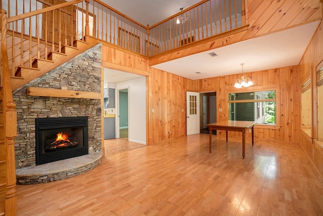 interior space with a fireplace, wooden walls, wood-type flooring, a high ceiling, and an inviting chandelier