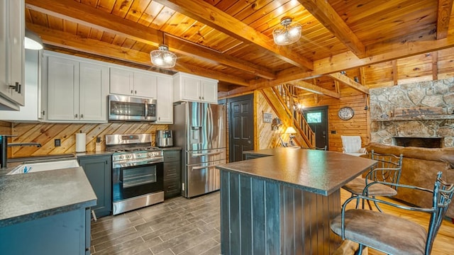 kitchen featuring appliances with stainless steel finishes, sink, white cabinets, beam ceiling, and wood walls