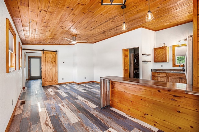 kitchen with a barn door, wooden ceiling, a sink, dark wood-style floors, and stacked washer and clothes dryer