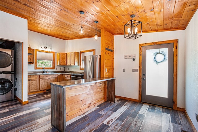 kitchen with dark wood-style flooring, decorative light fixtures, freestanding refrigerator, a sink, and stacked washing maching and dryer