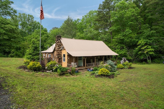 view of front of house with a porch, a front yard, a chimney, and a view of trees