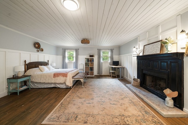 bedroom featuring a decorative wall, wooden ceiling, wood finished floors, wainscoting, and a fireplace with raised hearth