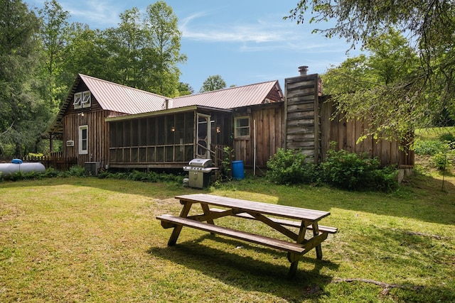 back of house with a sunroom, a lawn, and metal roof