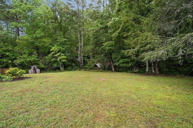view of grassy yard featuring a storage unit, an outdoor structure, and a wooded view