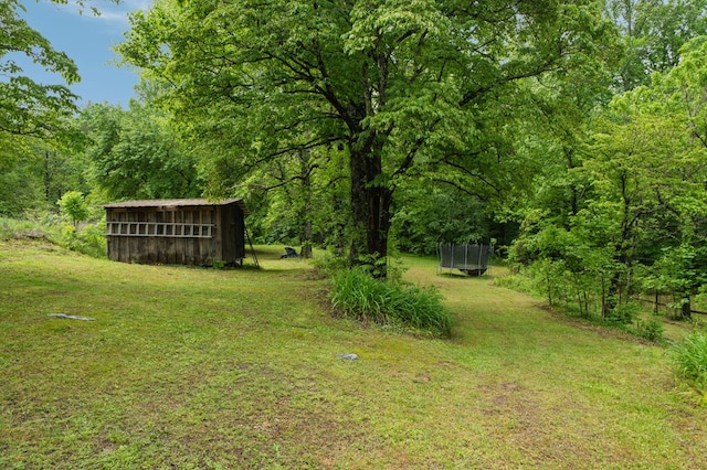 view of grassy yard featuring an outbuilding, a wooded view, and a trampoline