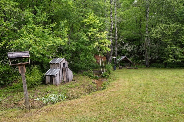 view of green lawn with a wooded view, a storage unit, and an outbuilding