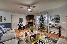 living room with hardwood / wood-style flooring, a stone fireplace, and ceiling fan