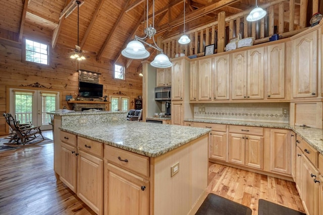 kitchen with light brown cabinetry, hanging light fixtures, wooden walls, and light stone countertops