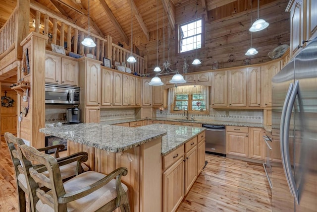 kitchen with light brown cabinetry, hanging light fixtures, stainless steel appliances, and light stone countertops