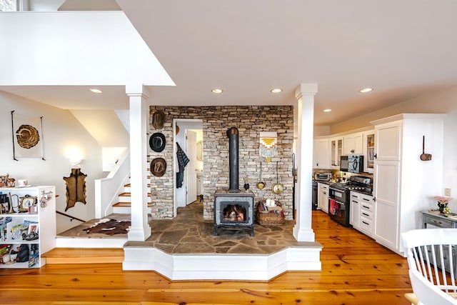 living room with light hardwood / wood-style floors, decorative columns, and a wood stove