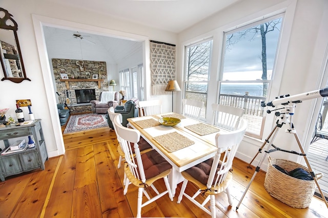 dining area with a water view, wood-type flooring, vaulted ceiling, ceiling fan, and a fireplace