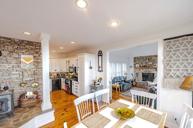 dining space featuring a stone fireplace, light hardwood / wood-style flooring, and decorative columns