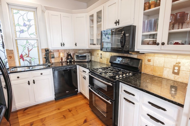 kitchen with sink, white cabinets, dark stone counters, black appliances, and light wood-type flooring