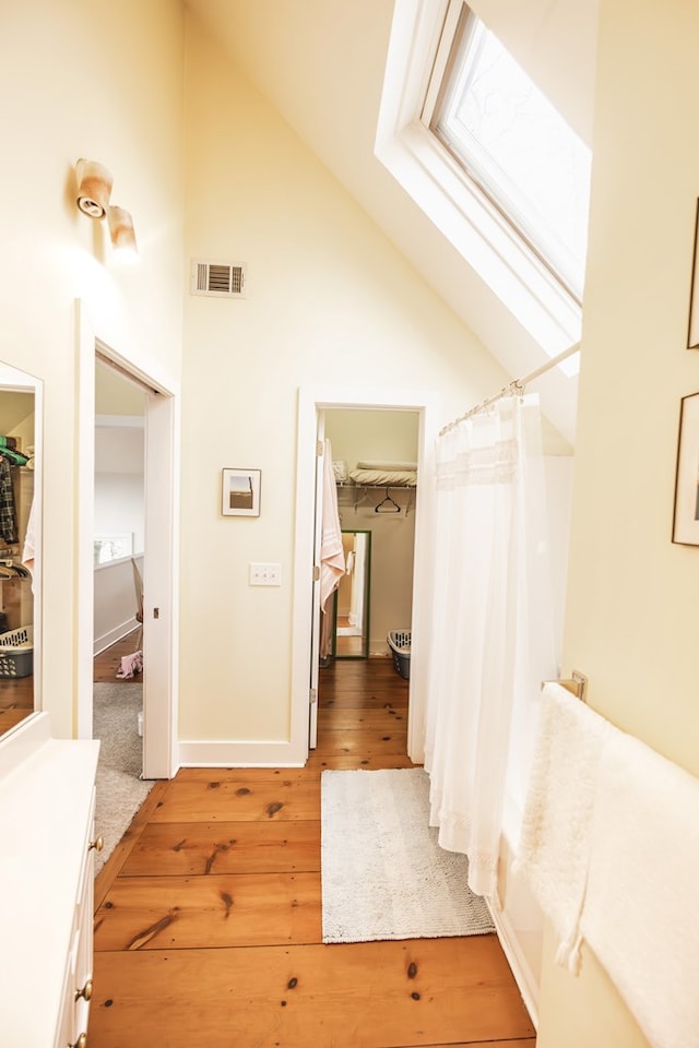 bathroom with high vaulted ceiling, a skylight, hardwood / wood-style flooring, vanity, and a shower with curtain