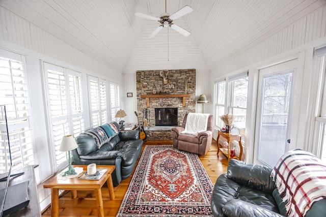 living room featuring ceiling fan, a stone fireplace, vaulted ceiling, and wood-type flooring