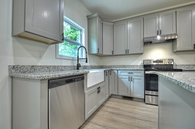 kitchen featuring appliances with stainless steel finishes, light stone counters, light wood finished floors, gray cabinets, and under cabinet range hood