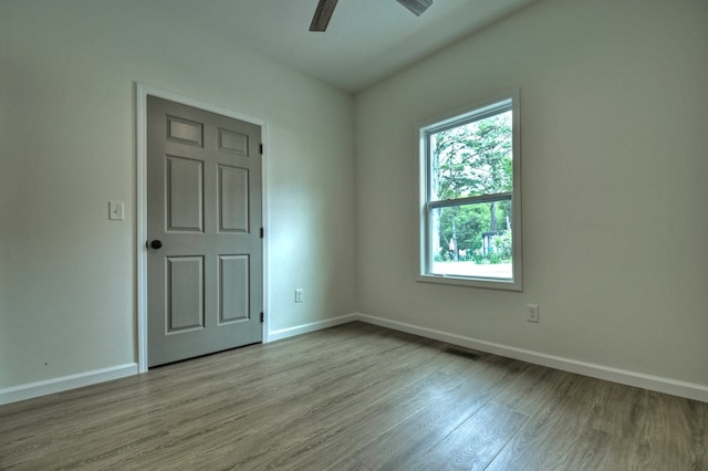 empty room with baseboards, a ceiling fan, wood finished floors, and visible vents