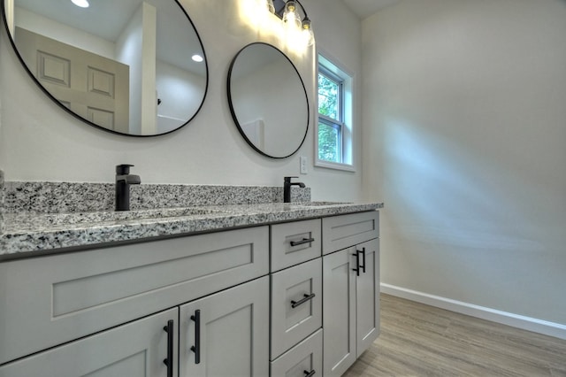 bathroom with a sink, baseboards, double vanity, and wood finished floors