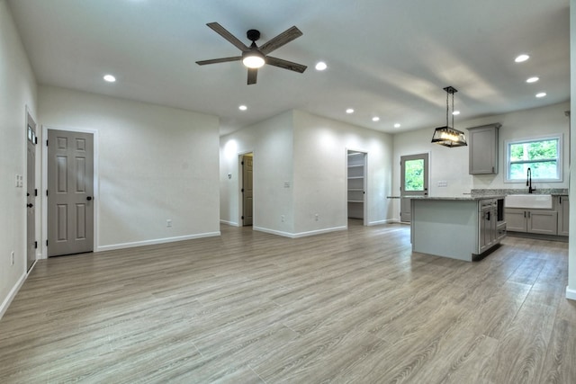 unfurnished living room featuring ceiling fan, a sink, baseboards, light wood-style floors, and recessed lighting