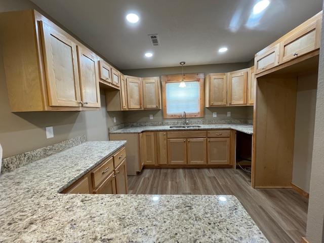 kitchen featuring hardwood / wood-style floors, pendant lighting, light stone counters, and sink