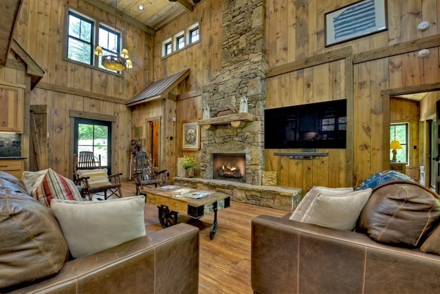 living room with a fireplace, a towering ceiling, wooden walls, and light wood-type flooring