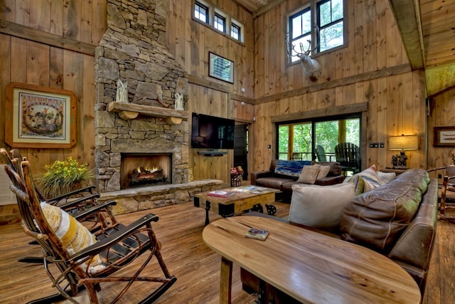 living room featuring light hardwood / wood-style flooring, a fireplace, a towering ceiling, and wooden walls