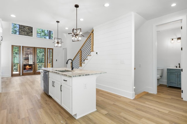 kitchen with light stone countertops, white cabinetry, pendant lighting, a center island with sink, and light wood-type flooring